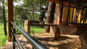 A stone-tiled patio with a metal railing, surrounded by trees and a brick structure. - Cabin, located in a natural area around (Mazamitla)