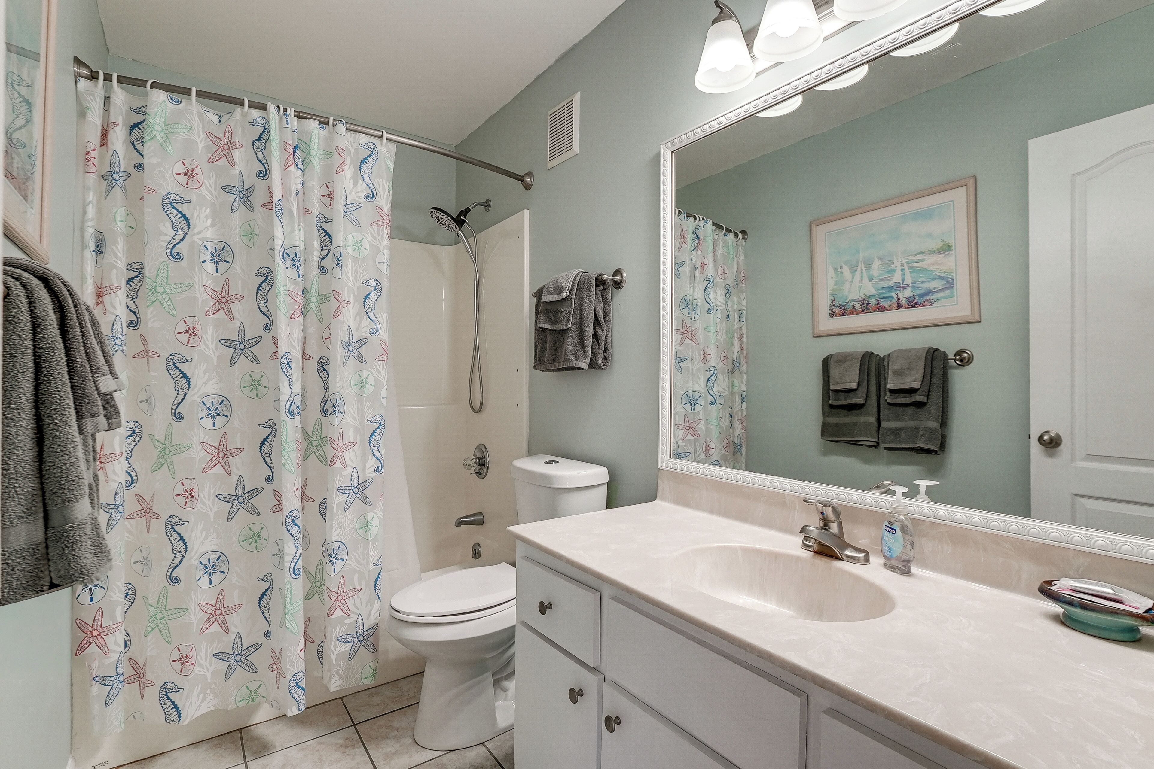 A bathroom with a shower curtain, toilet, sink, and mirror.