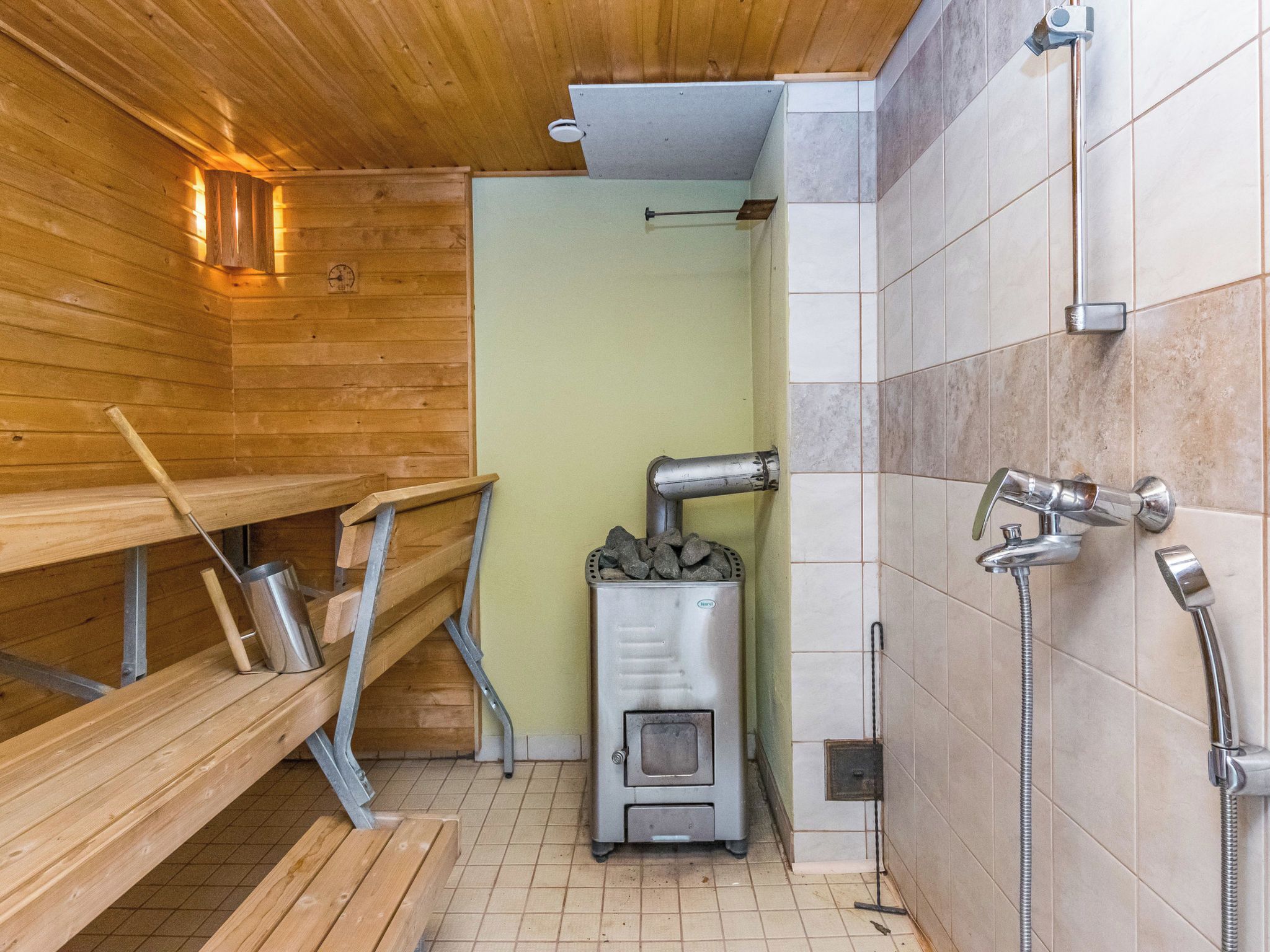 Une salle de sauna avec des bancs en bois, un appareil de chauffage pour sauna et un espace douche.