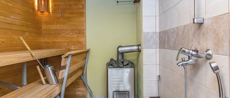 Ein Saunaraum mit Holzbänken, einer Saunaanlage und einem Duschbereich.