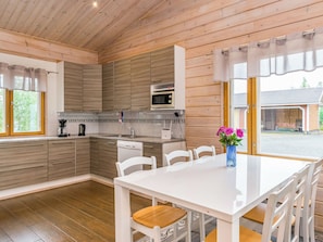 A modern kitchen with wooden cabinets, a white countertop, and a dining area with a white table and chairs. - Aurinkoranta by Interhome (Kitee)