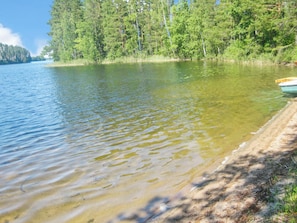A calm lake with clear water, surrounded by dense green trees and a sandy shore.