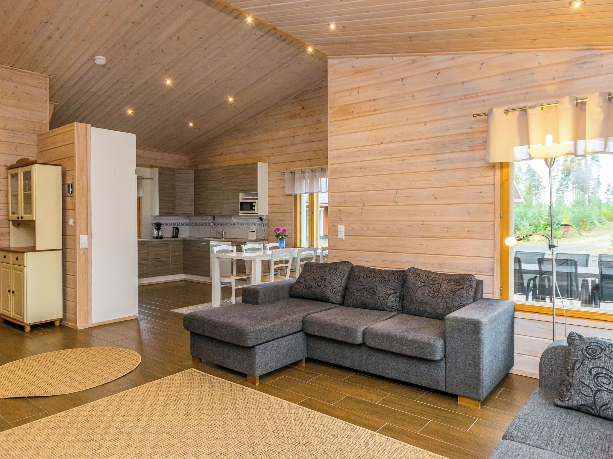 Ein modernes Interieur einer Blockhütte mit einem grauen Ecksofa, einer Küchenzeile und einem Essbereich.