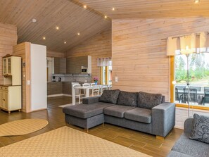 A modern log cabin interior with a grey sectional sofa, a kitchen area, and a dining space.