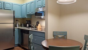 Cocina compacta con armarios color turquesa, electrodomésticos de acero inoxidable y una mesa de comedor de madera con sillas.