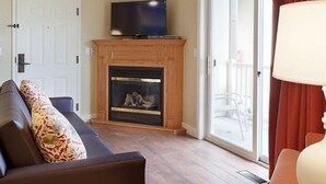 Un salón con chimenea, un televisor encima, un sofá con cojines estampados y vistas al exterior.