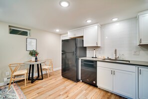 A modern kitchen with white cabinets, a black refrigerator, and a dining area with two chairs and a table. - Alluring Anchorage Apt - Walk to Coastal Trl! (Anchorage)