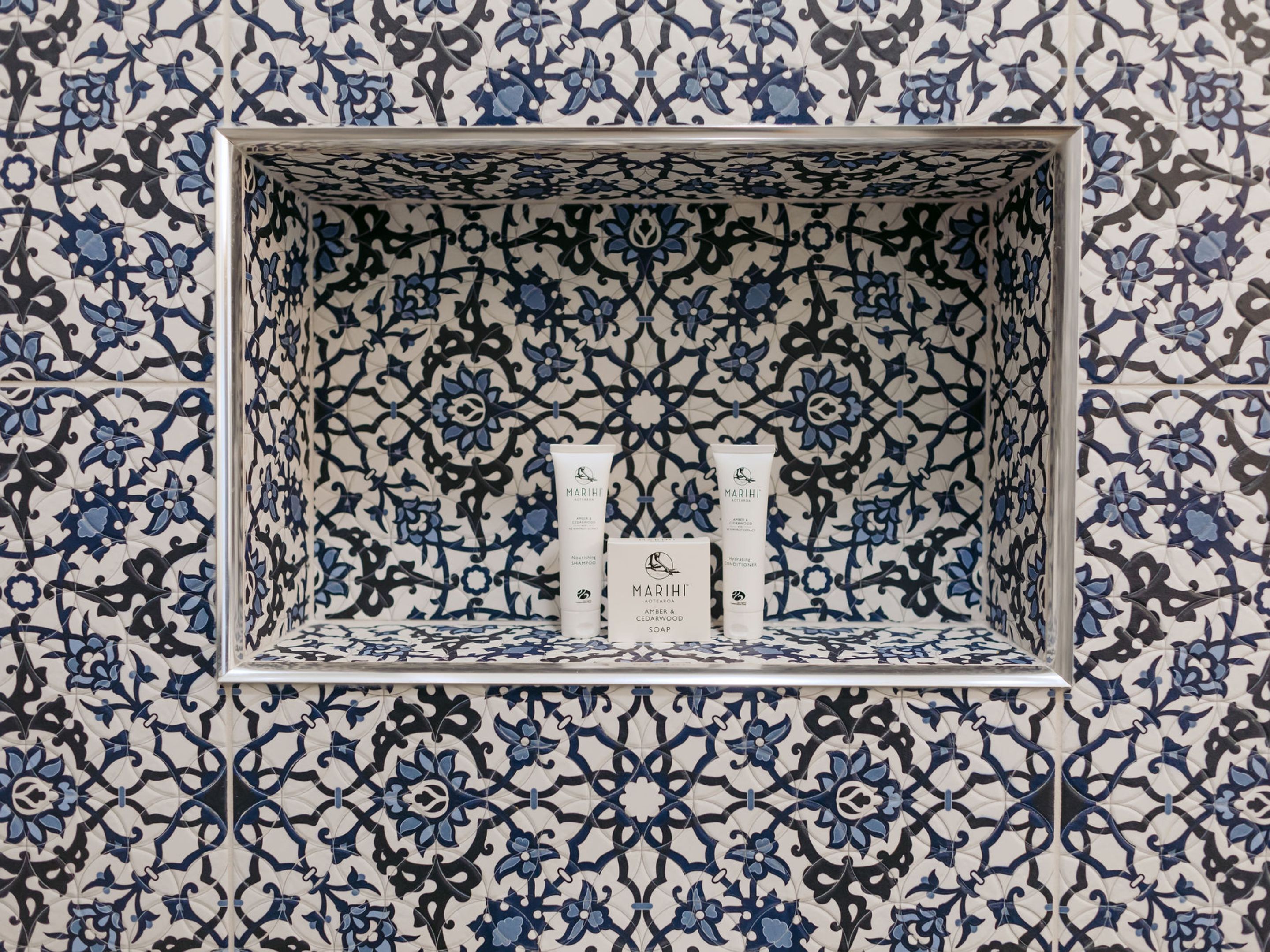 A bathroom with a tiled wall featuring a blue and white floral pattern. There is a shelf with two bottles of Mariti soap and a box of Mariti body wash.
