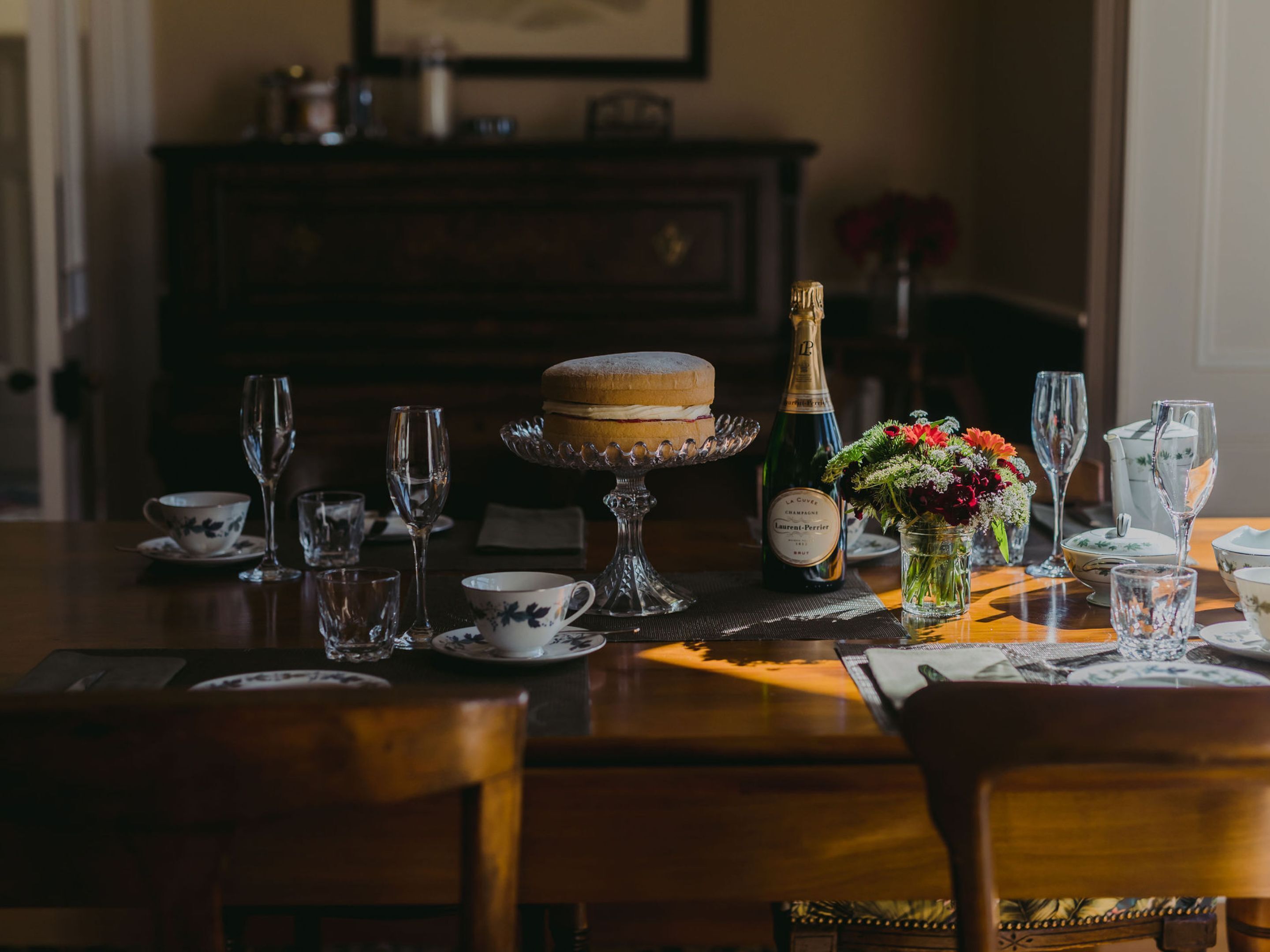 A dining table set with a cake, champagne, and flowers.