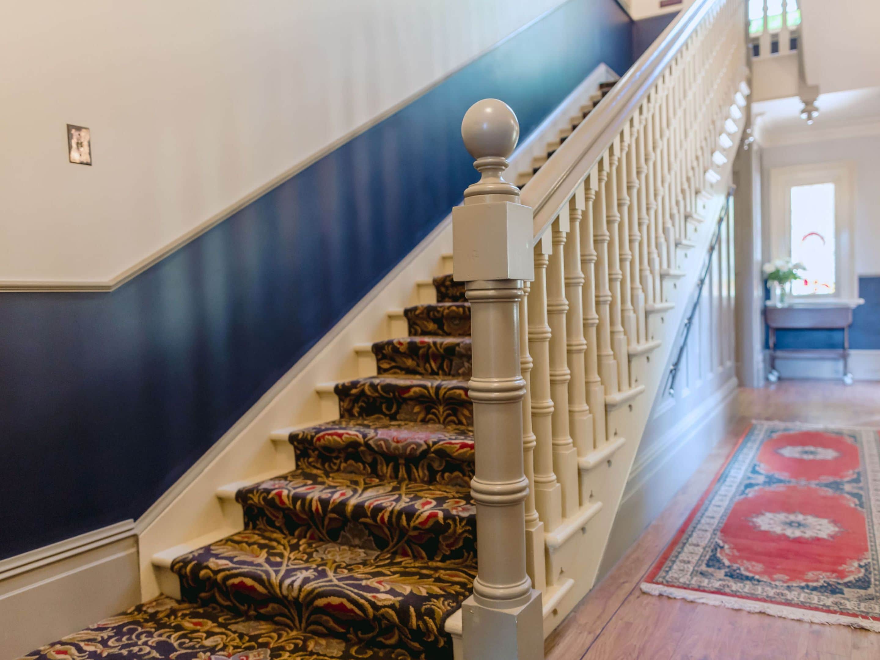 Una escalera con peldaños alfombrados y barandilla blanca ornamentada.