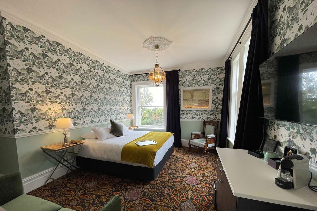 Una habitación de hotel con cama, escritorio, silla, televisión y ventana con cortinas.