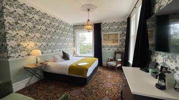 Habitación de hotel con cama, escritorio, silla, televisor y ventana con cortinas.