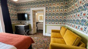 Ett hotellrum med en säng, en gul fåtölj, ett skrivbord med en tv och ett badrum som syns genom en öppen dörr.