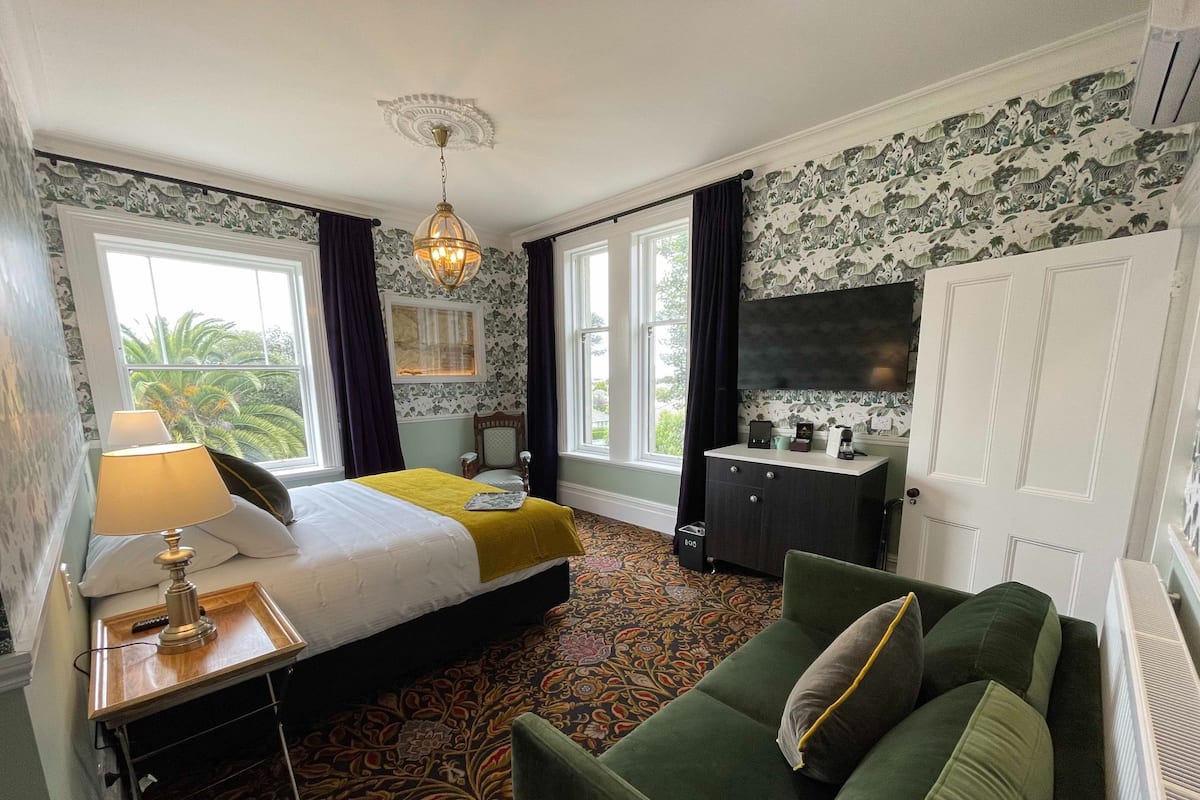 Habitación de hotel con cama, sofá verde, escritorio con lámpara, cómoda y televisor.