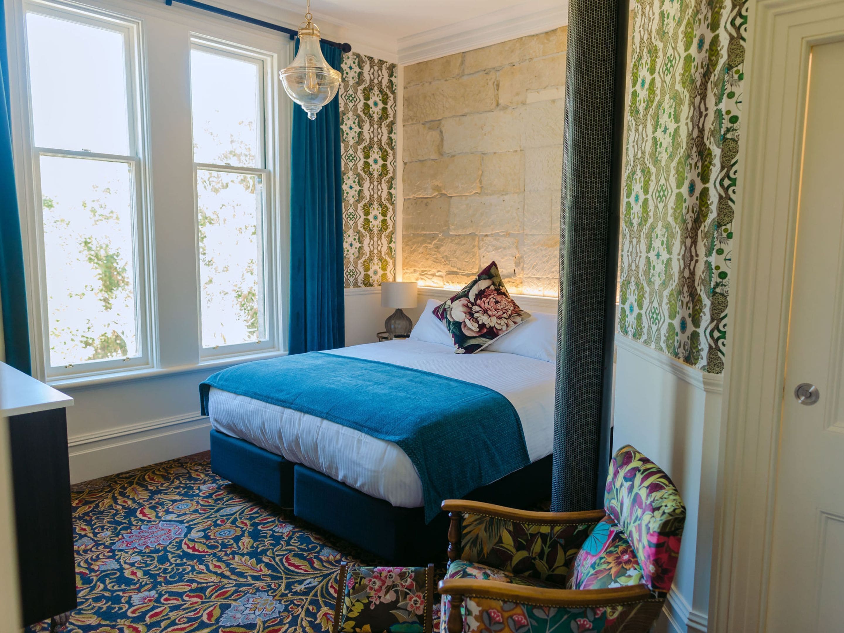 A bedroom with a large bed, a chair, a window, and a patterned carpet.