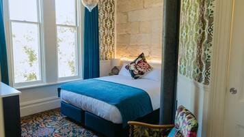 A bedroom with a large bed, a chair, a window, and a patterned carpet.