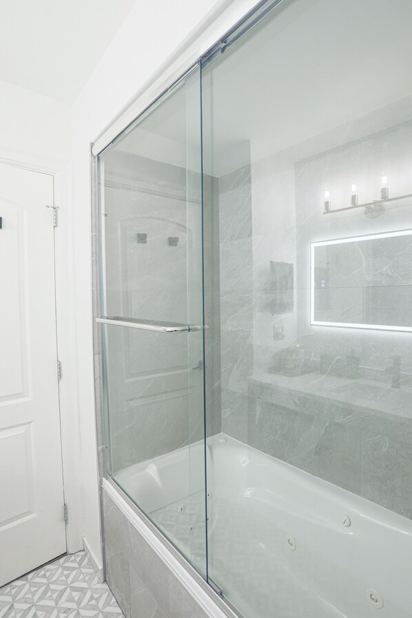 Een moderne badkamer met een douchecabine van glas, een witte deur en een vloer van marmer.