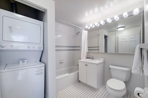A bathroom with a washing machine, a bathtub, a toilet, and a vanity with a mirror.