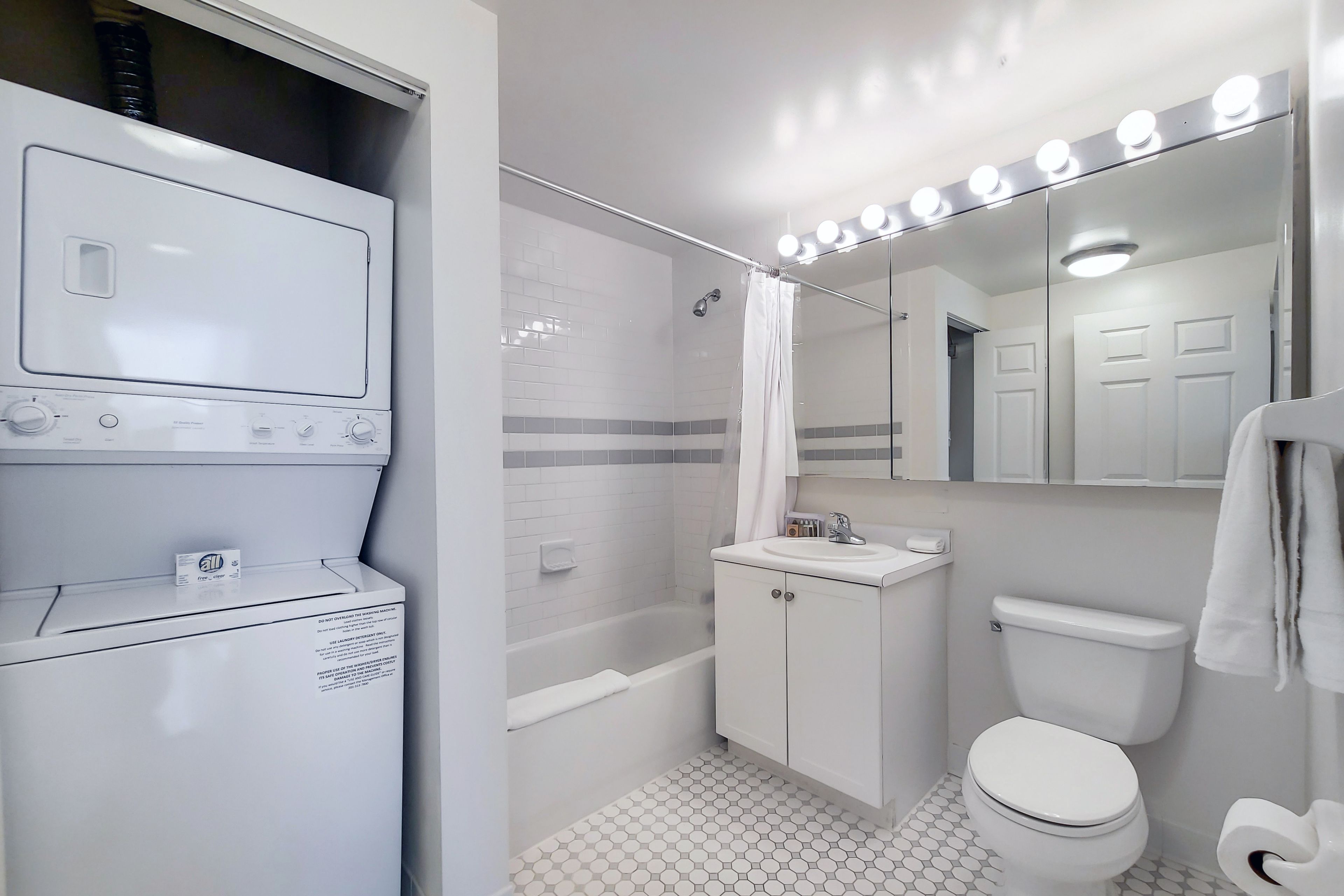 Une salle de bain équipée d’un lave-linge, d’une baignoire, de toilettes et d’un meuble-lavabo avec un miroir.