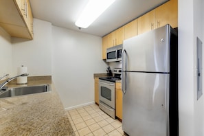 A compact kitchen with a stainless steel refrigerator, microwave, oven, and a sink with a faucet.