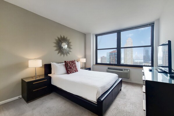 A modern hotel room with a large window, a bed, a desk, and a nightstand.