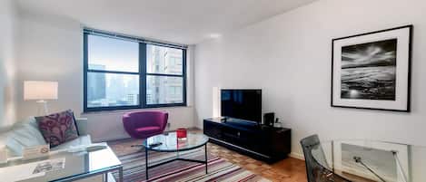 A modern living room with a sofa, a glass coffee table, a purple chair, a TV, and a framed picture on the wall.