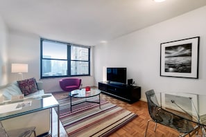 A modern living room with a sofa, a glass coffee table, a purple chair, a TV, and a framed picture on the wall.