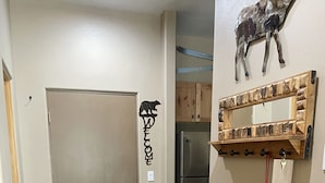 A hallway with a stone-tiled floor, a wooden bench, a refrigerator, a coat rack, and a 'Welcome' sign.