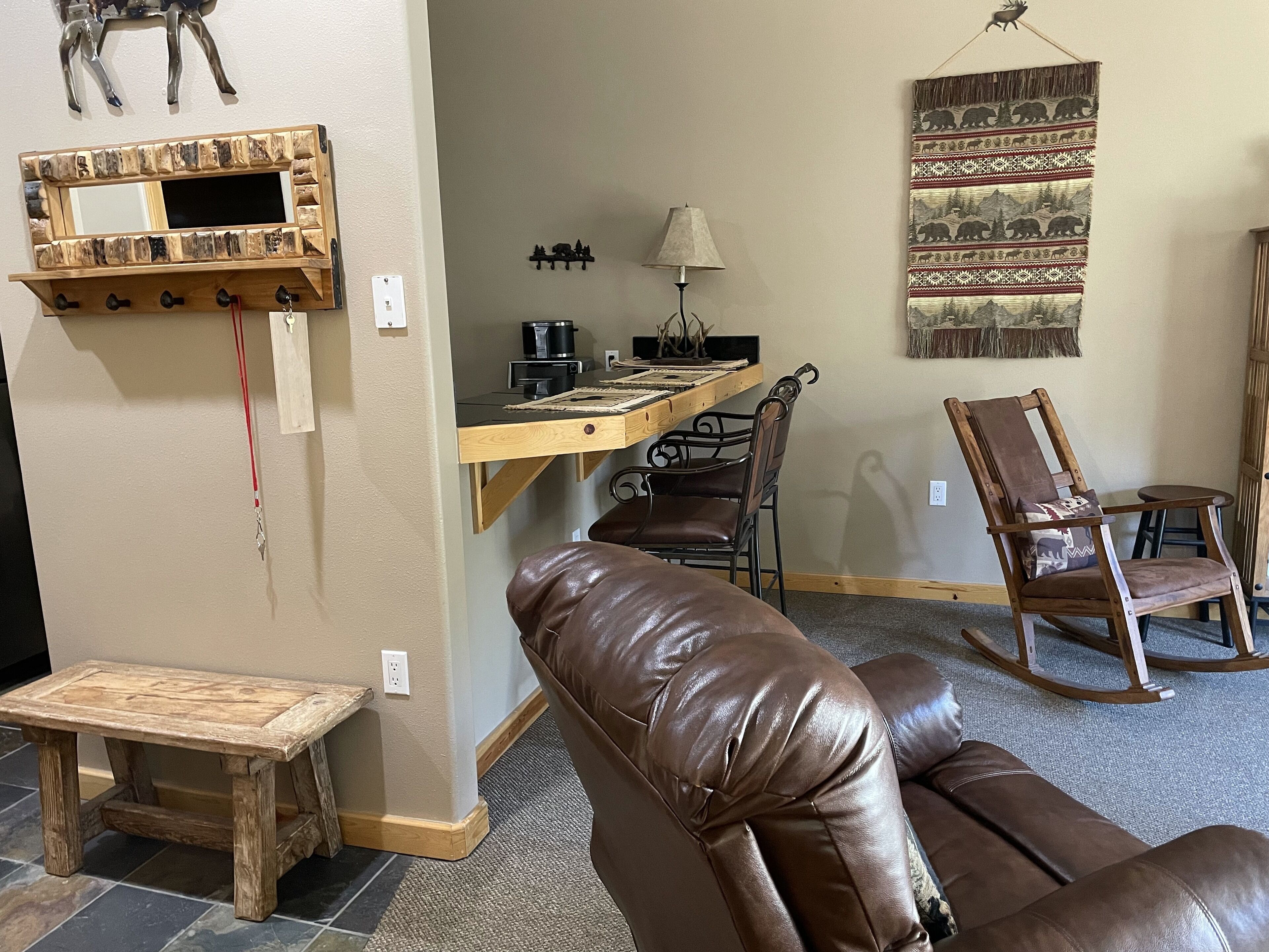 Un salon chaleureux avec un canapé en cuir marron, une table basse en bois, un petit banc en bois, un coin repas avec une table et des chaises en bois, et un miroir fixé au mur.