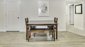 Un coin repas avec une table et des bancs en bois, une porte blanche et une œuvre d’art encadrée au mur.