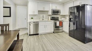 Une cuisine moderne avec des meubles blancs, des appareils en acier inoxydable et une table à manger en bois.