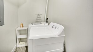 Un espace buanderie compact comprenant un lave-linge blanc, une petite étagère avec des vêtements pliés et un porte-serviettes.