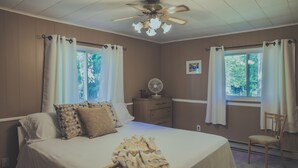 Une chambre avec un grand lit, un ventilateur de plafond, une table de chevet avec un ventilateur et une chaise.
