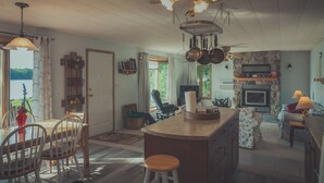 Une cuisine spacieuse avec un îlot central, des chaises en bois et une table à manger. On y trouve également un ventilateur de plafond, une fenêtre avec des rideaux et une cheminée en pierre.