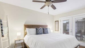 A bedroom with a large bed, a ceiling fan, a nightstand, and a view through a glass door.
