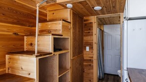 A compact wooden cabin with a kitchenette, a door leading to a bathroom, and a small shelf unit.