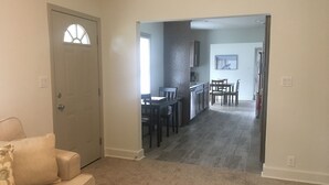 Una sala de estar con un sofá color crema, un comedor con mesa y sillas, y una cocina con armarios y encimera.