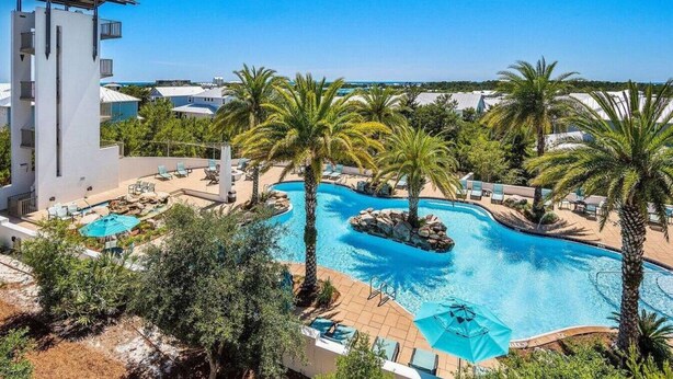 Un complexe hôtelier doté d’une grande piscine, entourée de palmiers et de chaises longues.