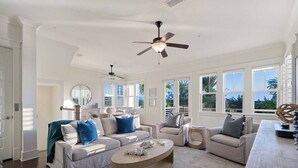 Un salon spacieux doté d’un ventilateur de plafond, de grandes fenêtres et offrant une vue sur l’extérieur.