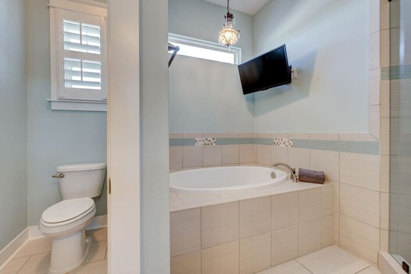 Un bagno con un water, una vasca e una TV fissata al muro.