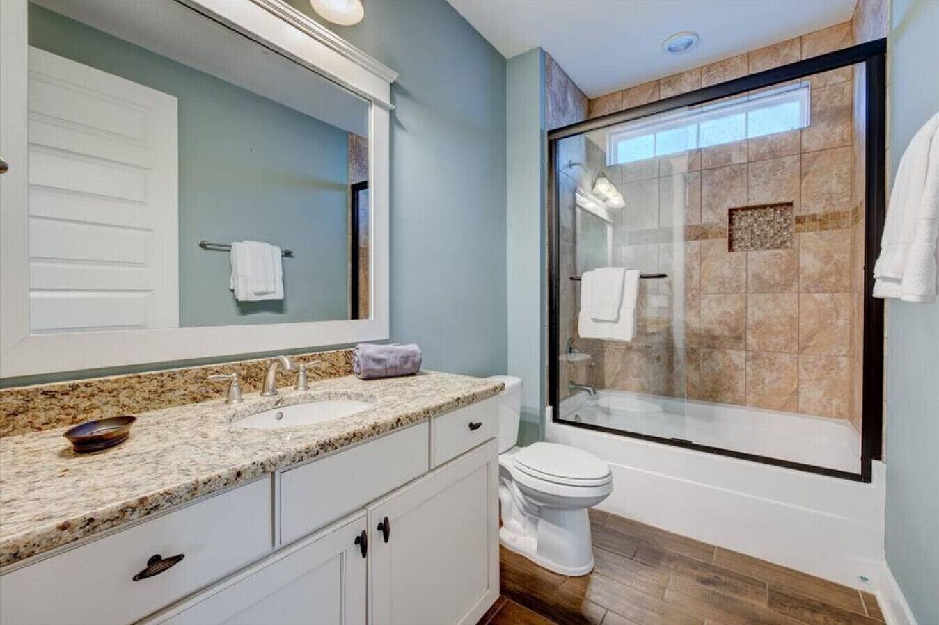 A bathroom with a double sink, a large mirror, a glass shower enclosure, and a toilet.