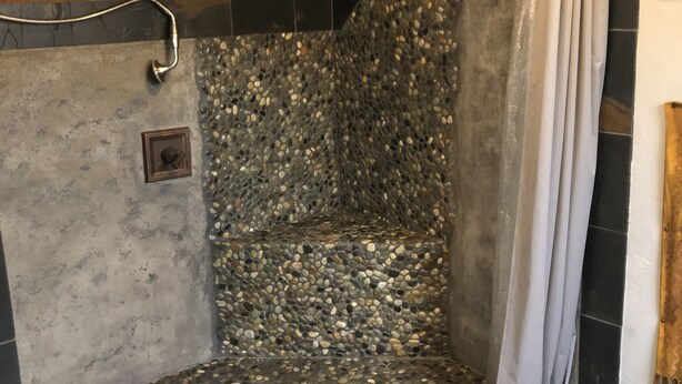 Chuveiro com parede em mosaico de pedras, teto de madeira e cortina de chuveiro.