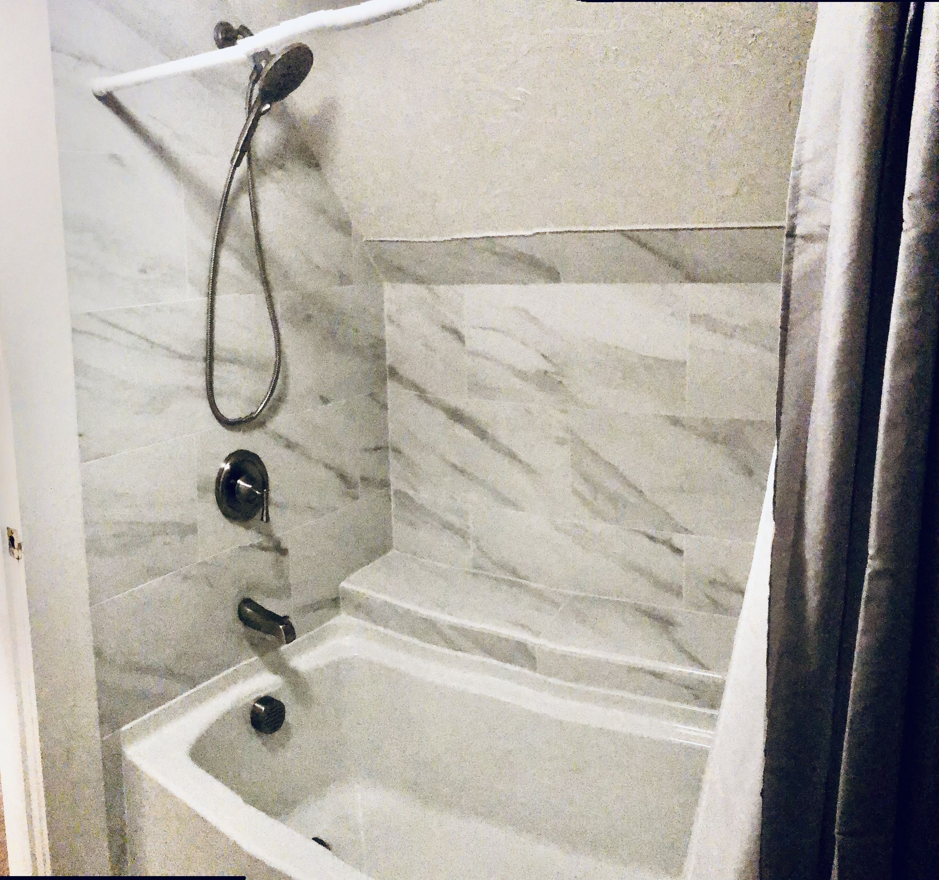 Un baño con pared de mármol, una bañera y un cabezal de ducha.