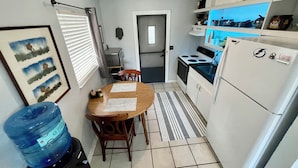 Una cocina compacta con una mesa de comedor, sillas, dispensador de agua y un refrigerador.