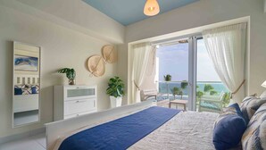 Un dormitorio con una cama grande, vista al océano, un balcón con mesa y sillas, e iluminación en el techo.