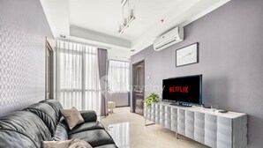 Een moderne woonkamer met een leren bank, een tv op een witte console en een groot raam met gordijnen.