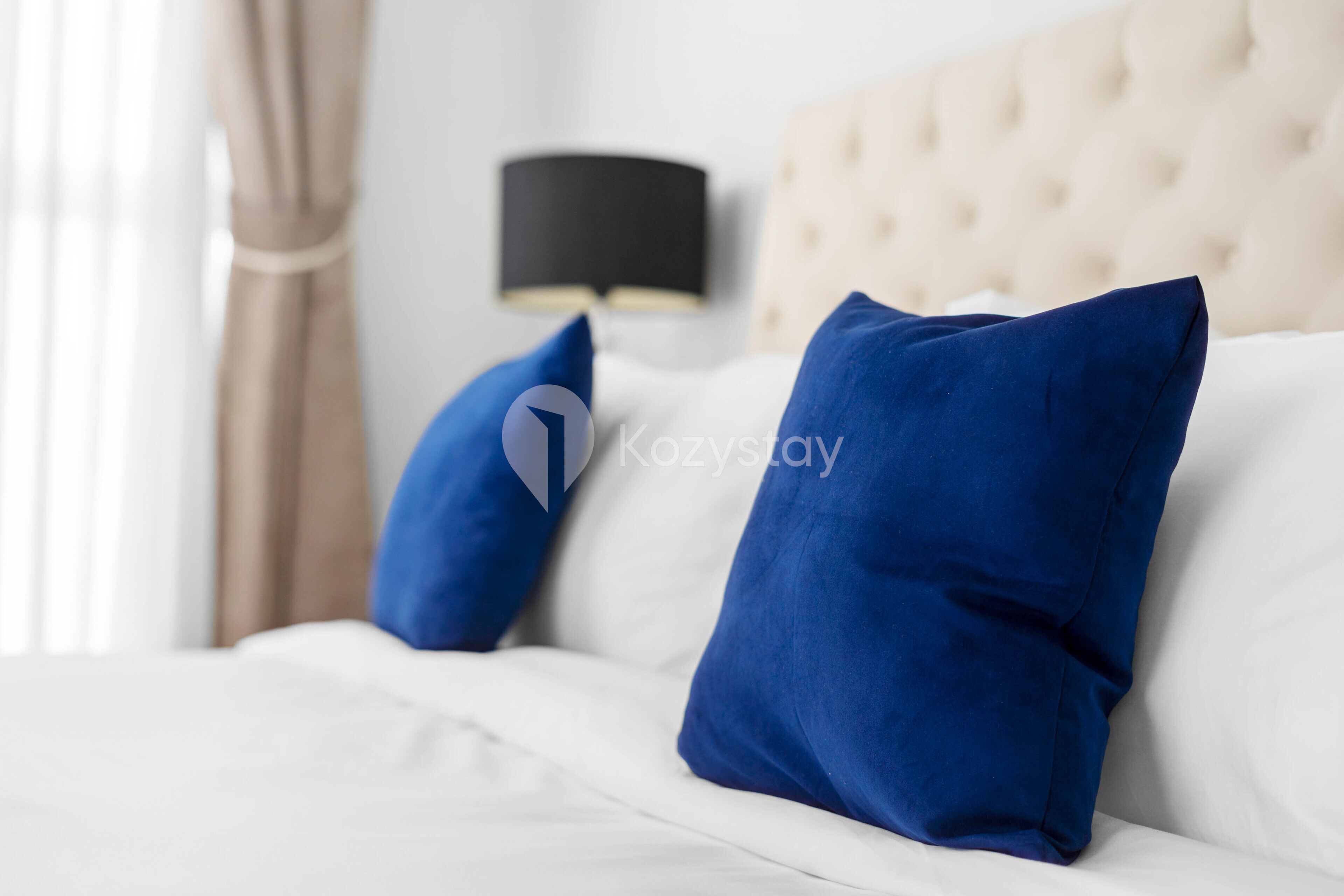 A bed with white bedding and two blue pillows.