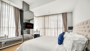 A modern hotel room with a large bed, a flat-screen TV, a bedside table, and a large window with curtains. - CASTILLE by Kozystay (Jakarta)