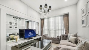 A modern living room with a flat-screen TV, a glass coffee table, a grey sofa, and a chandelier. - CASTILLE by Kozystay (Jakarta)
