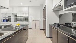 A modern kitchen with black countertops, a stove, and a sink. There is a refrigerator and cabinets in the background. - CASTILLE by Kozystay (Jakarta)